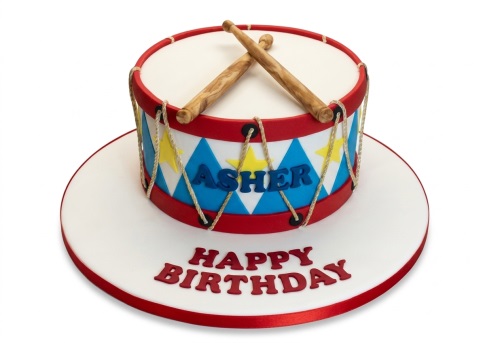 Round drum shaped birthday cake with drumsticks, red, white, blue harlequin pattern, and yellow stars.
