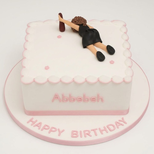 White square birthday cake with pink trim and an edible figure of a woman lying down holding a bottle.