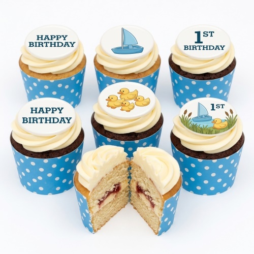 Vanilla and chocolate cupcakes with white icing, blue polka dot wrappers, and toppers featuring ducks, sailboats, and '1st Birthday' messages.