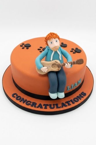Orange round cake with a male musician figure playing guitar, paw prints, and custom message.