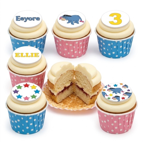 Eeyore themed birthday cupcakes with white frosting, blue and pink polka dot wrappers, and custom age and name toppers.