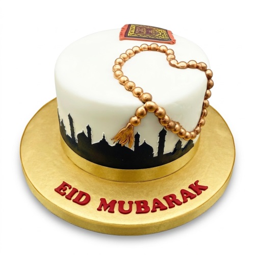 White Eid Mubarak cake with gold prayer beads, prayer mat, and black mosque silhouette.