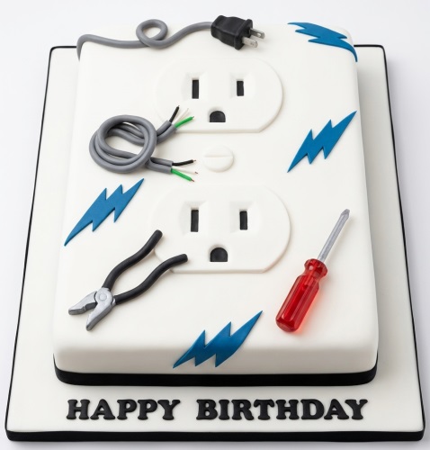 White rectangular cake decorated with edible power outlets, wires, plug, pliers, screwdriver, and blue lightning bolts, with 'Happy Birthday' written at the base.