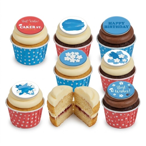 Assorted celebration cupcakes with blue and red polka dot cases, topped with white frosting and edible designs including 'Happy Birthday' and floral patterns.