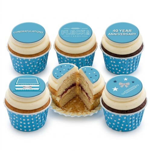 Six celebration cupcakes with blue and white polka dot wrappers, white frosting, and blue customisable toppers.
