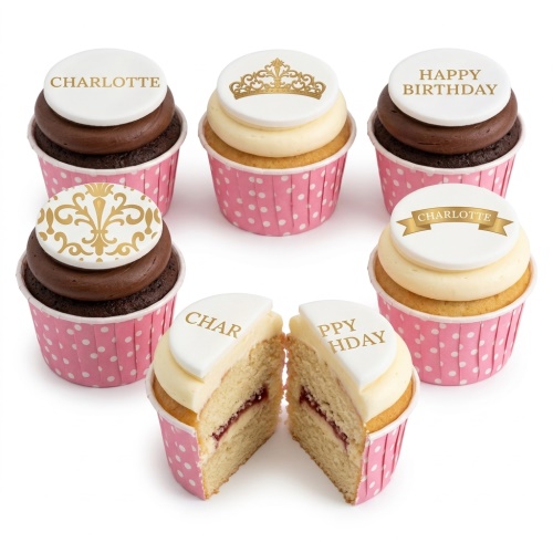 Assortment of elegant birthday cupcakes with gold crown and ornate designs on white fondant toppers, in pink polka dot wrappers.