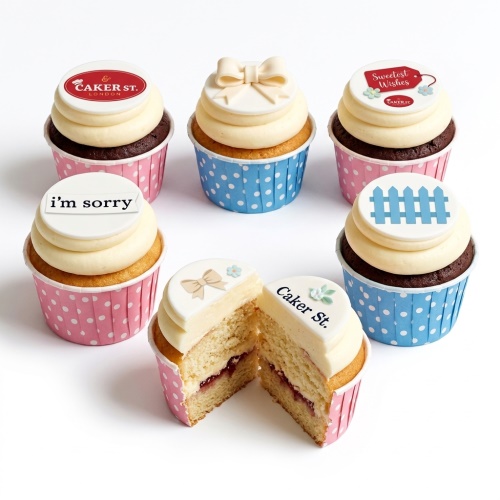 A selection of personalised cupcakes with white frosting, pink and blue polka dot wrappers, and edible toppers featuring bows, a fence, and custom messages.
