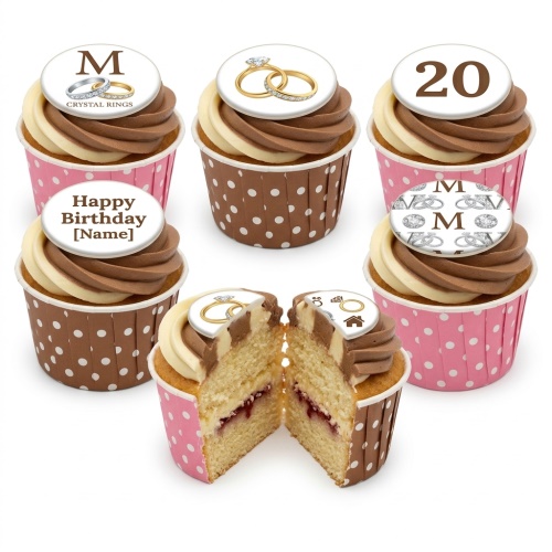 Cupcakes with swirled cream and chocolate frosting, topped with edible engagement rings, initial 'M', and number '20' designs, in pink and brown polka dot wrappers.