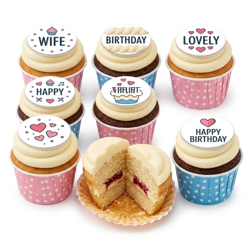 Selection of birthday cupcakes with white frosting, pink and blue polka dot wrappers, and white toppers with messages like 'WIFE', 'BIRTHDAY', 'LOVELY', 'HAPPY', and hearts. One cupcake is cut open showing jam filling.