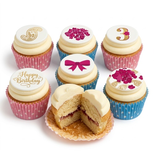 Six cupcakes with cream frosting, decorated with white edible toppers featuring gold paisley, fuchsia floral patterns, a pink bow, "Happy Birthday" script, and a gold number '3'. One cupcake is cut in half revealing jam filling.