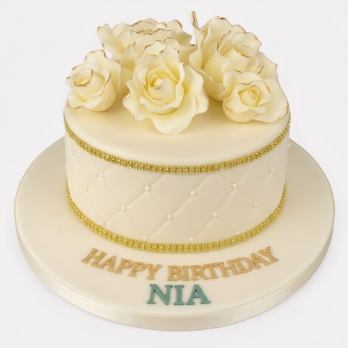 Round cream birthday cake with gold trim, quilted pattern, and cream roses with gold edges.