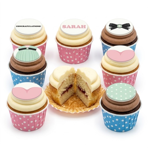 Selection of elegant cupcakes with cream and chocolate frosting, topped with a black bow, mint green dress, pink heart, and polka dots.