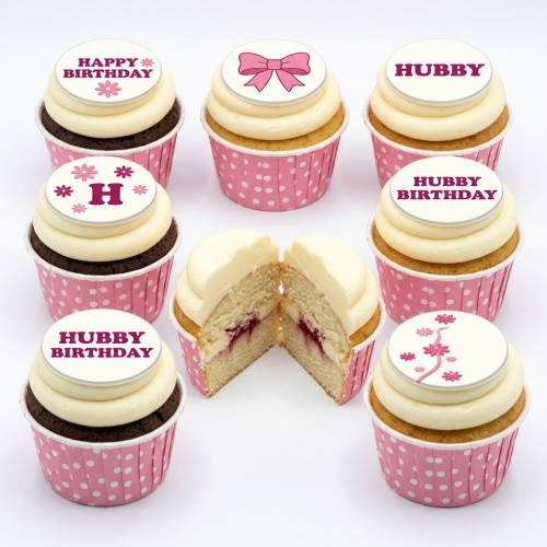 A selection of personalised birthday cupcakes with white frosting, pink polka dot wrappers, and pink bow and floral toppers.