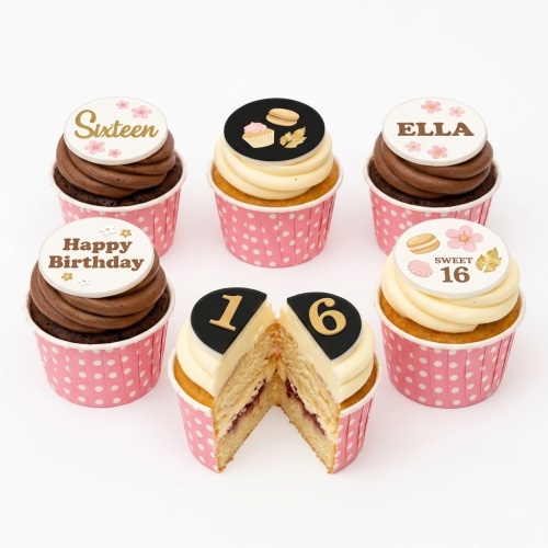 Set of six elegant floral birthday cupcakes with pink polka dot wrappers, white and chocolate frosting, and various customisable toppers including flowers, macarons, and numbers.