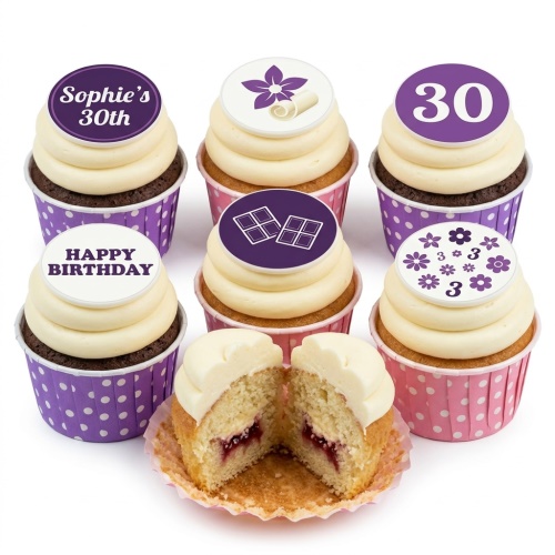 Assortment of birthday cupcakes with white frosting, purple and pink wrappers, decorated with floral, chocolate, and custom age toppers.