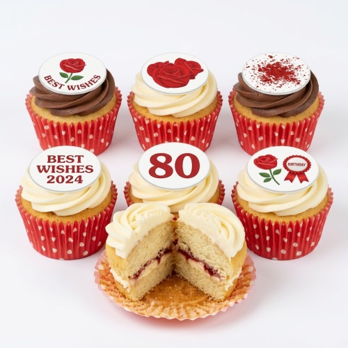 Six cupcakes with red rose and birthday themed edible toppers, some with chocolate and vanilla frosting, in red polka dot wrappers. One cupcake is cut open showing jam filling.