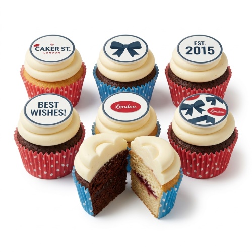 Six celebration cupcakes with cream frosting, bow designs, and custom message toppers in red and blue cases.