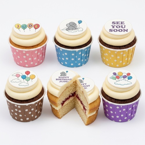 Cupcakes with white frosting and edible toppers featuring baby elephants, balloons, and clouds in colourful polka dot wrappers.