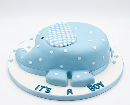 Blue elephant shaped cake with white polka dots and 'It's a Boy' message on the board.