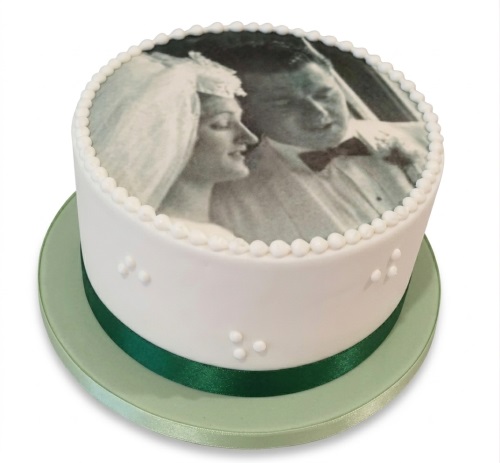 White round cake with an edible black and white wedding photo print on top, decorated with white pearls and a green ribbon.