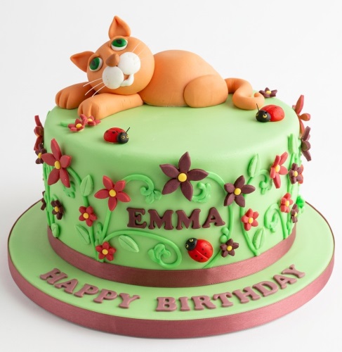 Green birthday cake with orange cat topper, red and brown flowers, green vines, and red ladybirds.