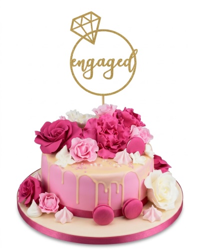 Pink engagement cake with floral decorations, macarons, and a gold 'engaged' topper.
