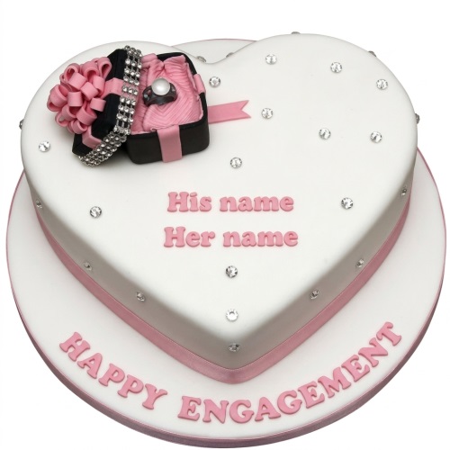 White heart-shaped engagement cake with pink ribbon, edible ring box, and scattered rhinestones.