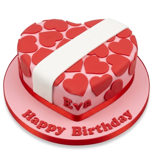 Heart-shaped pink birthday cake with red hearts, a white band, and a personalised message on the board.