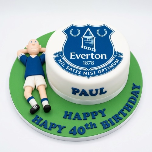 Round white cake with blue Everton FC crest, green board, and fondant football player figure.