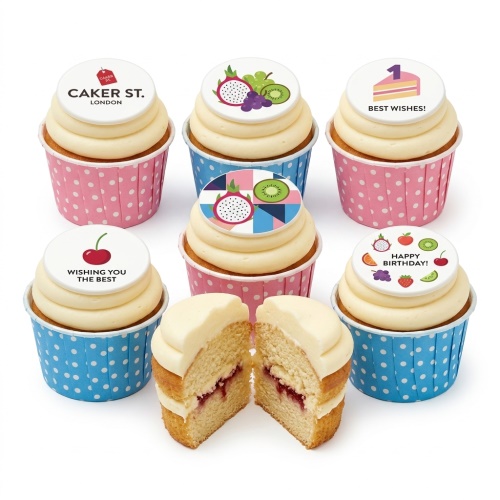 Assortment of vanilla cupcakes with white frosting and edible fruit-themed birthday toppers in pink and blue cases.