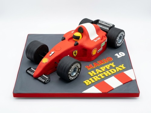 Red Formula 1 racing car cake on a grey board with white and red track markings.