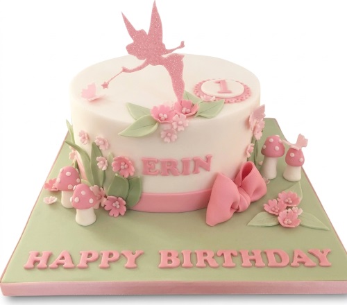 White round cake with pink glitter fairy, sugar flowers, mushrooms, and a pink bow.