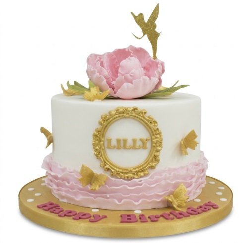White and pink fairy birthday cake with a large pink flower, gold butterflies, and a glitter fairy topper.