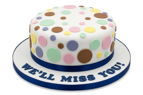 White round cake with colourful polka dots and a blue ribbon, featuring a custom message.