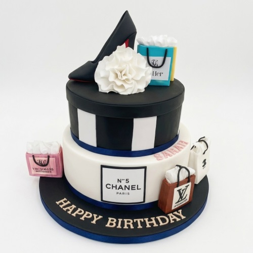 Two-tier designer fashion birthday cake with high heel shoe, sugar flower, and luxury shopping bags.