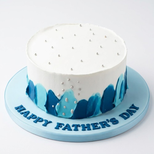Round white cake with blue brushstroke decoration, silver pearls, and 'Happy Father's Day' message.