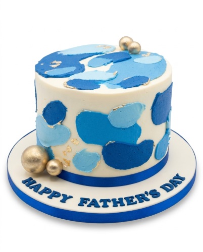 Round white cake with abstract blue patches, gold leaf, and gold spheres, with 'Happy Father's Day' on the base.