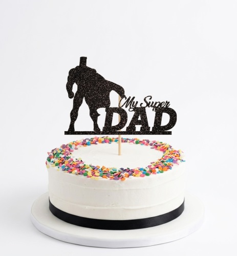 White single-tier cake with multi-coloured sprinkles and a black 'My Super DAD' superhero topper.