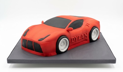 Red racing car birthday cake with black accents and white wheels, personalised with a custom name.