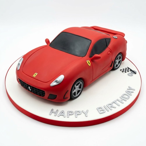 3D red Ferrari sports car birthday cake with silver wheels and a 'Happy Birthday' message on the board.