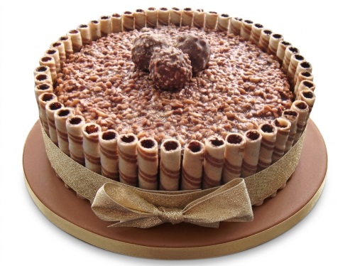 Round chocolate cake with crushed chocolate topping, three chocolate spheres, wafer rolls, and a gold ribbon bow.