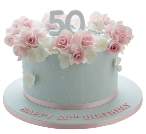Round pastel blue cake with pink roses, white flowers, polka dots, and a custom age topper.