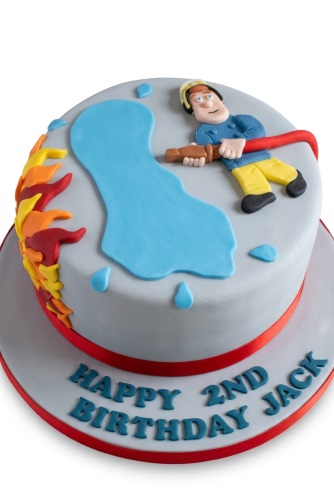 Round grey birthday cake with a 3D fondant Fireman Sam figure, red hose, blue water splash, and orange and red flames.