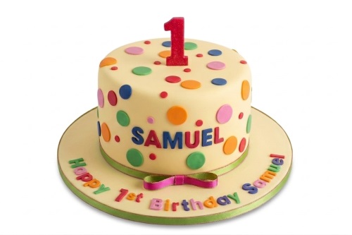 Round yellow 1st birthday cake with colourful polka dots and a red number one topper.