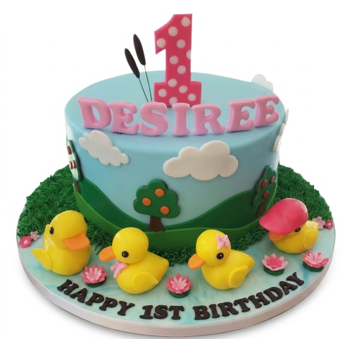 Round 1st birthday cake with yellow ducklings, pink number one topper, and a pond scene.