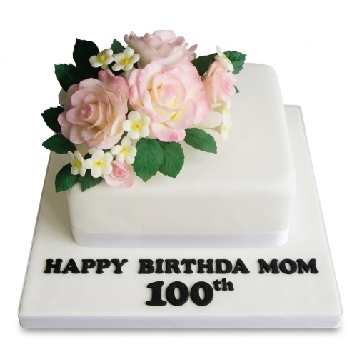 Two-tier white square cake with pink sugar roses, white flowers, green leaves, and a custom message board.