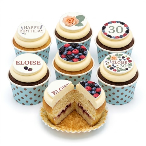 A selection of vanilla and chocolate cupcakes with cream frosting and various edible toppers including floral, berry, and custom age/name designs.