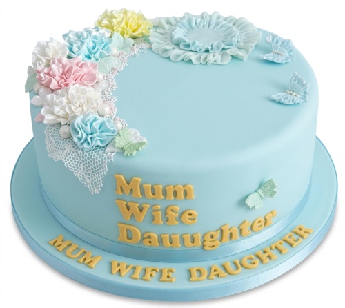 Light blue round cake with pastel fondant flowers, white lace, and butterflies, featuring a custom message.