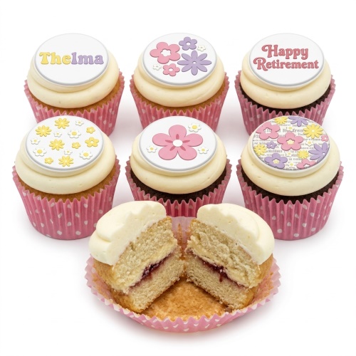 Assortment of floral cupcakes with cream frosting and pink polka dot wrappers, some with flower toppers, one cut open to show jam filling.