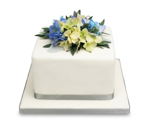 Elegant white square cake with blue and light green floral arrangement and silver ribbon.